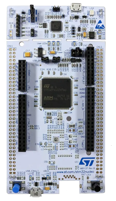 The image shows a circuit board labeled as "NUCLEO" with an ARM microcontroller at the center. Various components, including connectors, resistors, LEDs, and a USB port, are present across the board, providing interfaces for programming and power. The overall design is intended for development and experimentation.